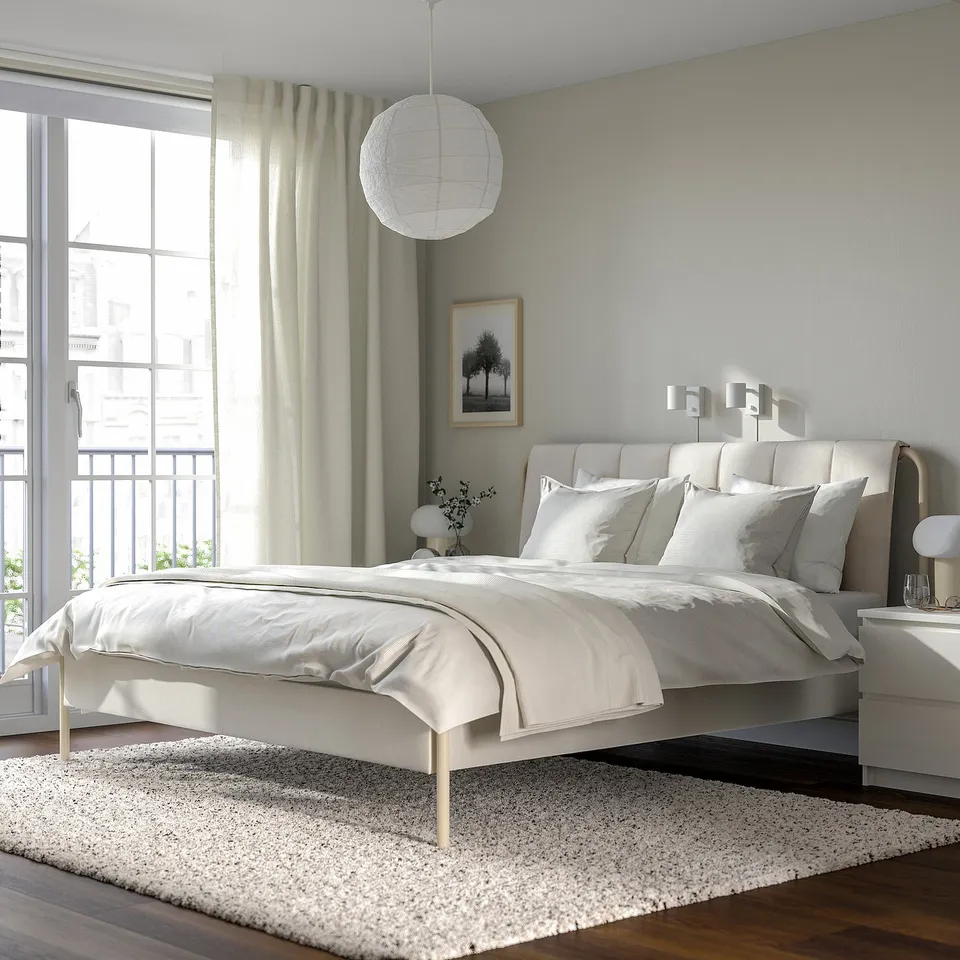 Modern bedroom with TÄLLÅSEN bed, light headboard, large window, white linens, small rug, bedside table, and lamp.