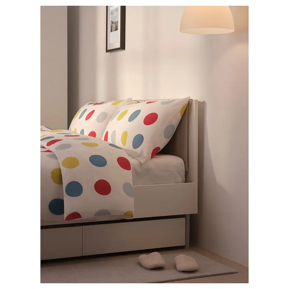 Bright polka dot bedding on white bed frame with cushioned headboard and wall lamp.