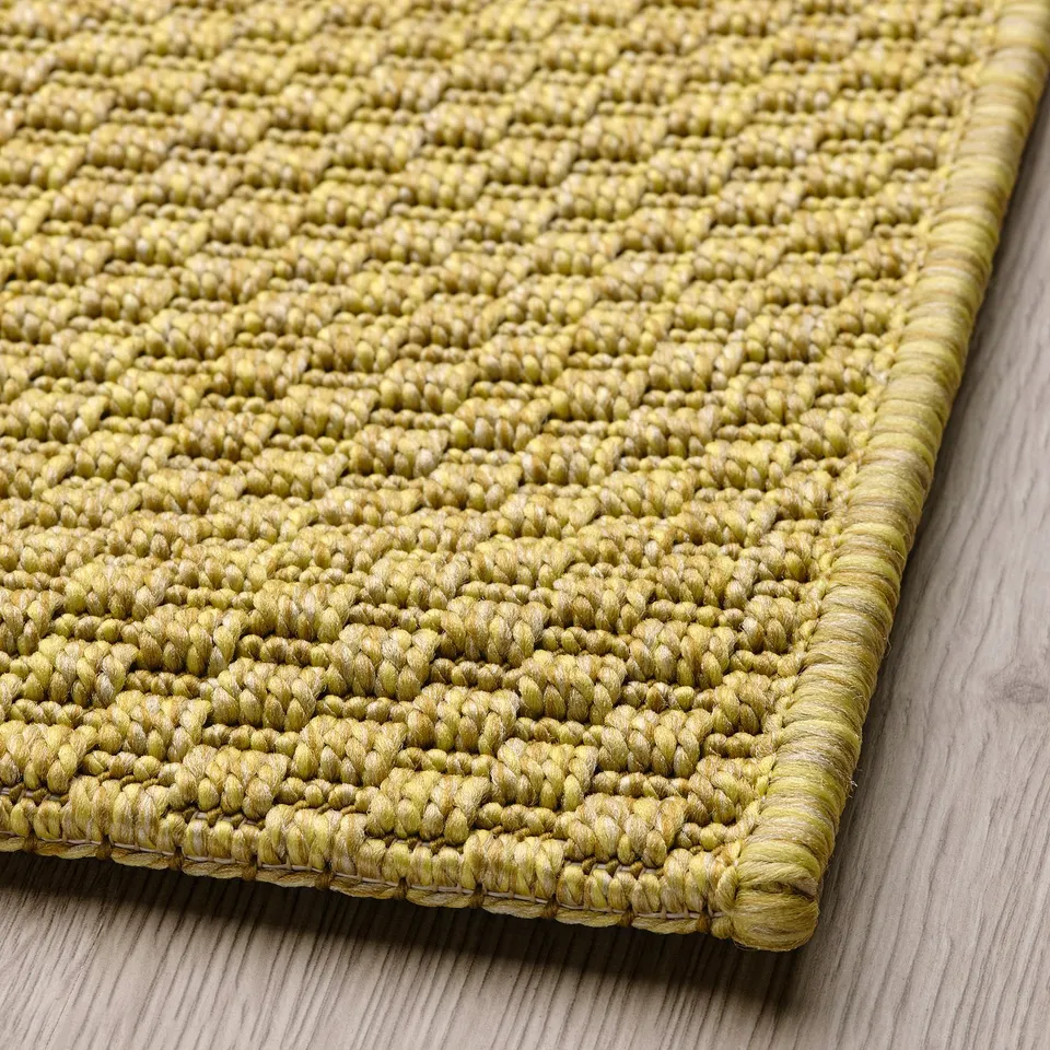 Close-up of green woven rug. Textured, tightly knit surface, resting on wooden floor. High quality, intricate weave.