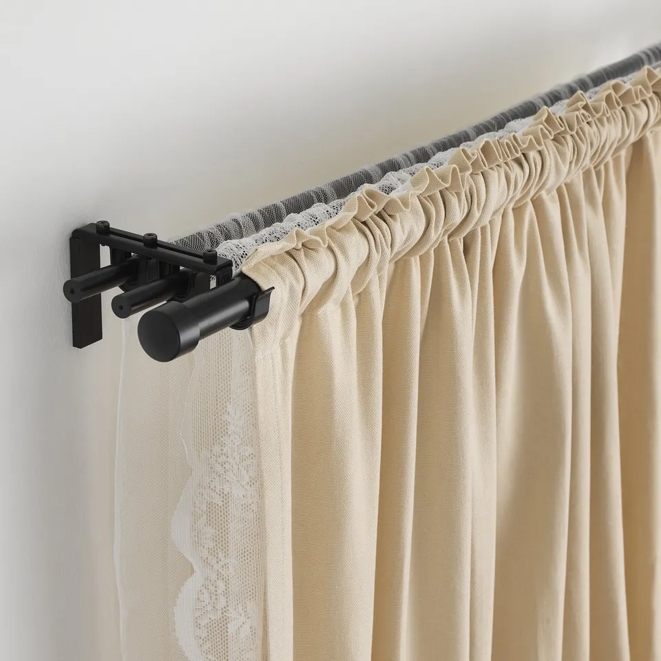 Triple curtain rod setup with pleated curtains on adjustable black rail.