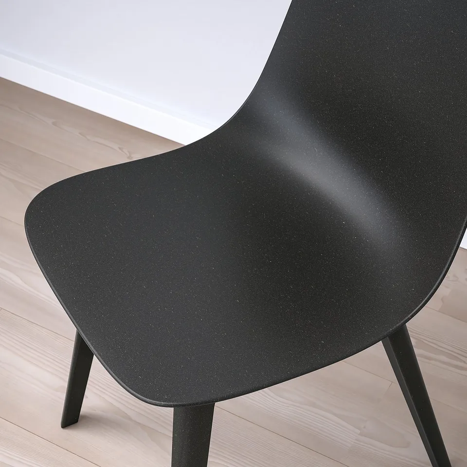 Black modern chair with sleek design on light wooden floor. High-quality materials, ergonomic shape.