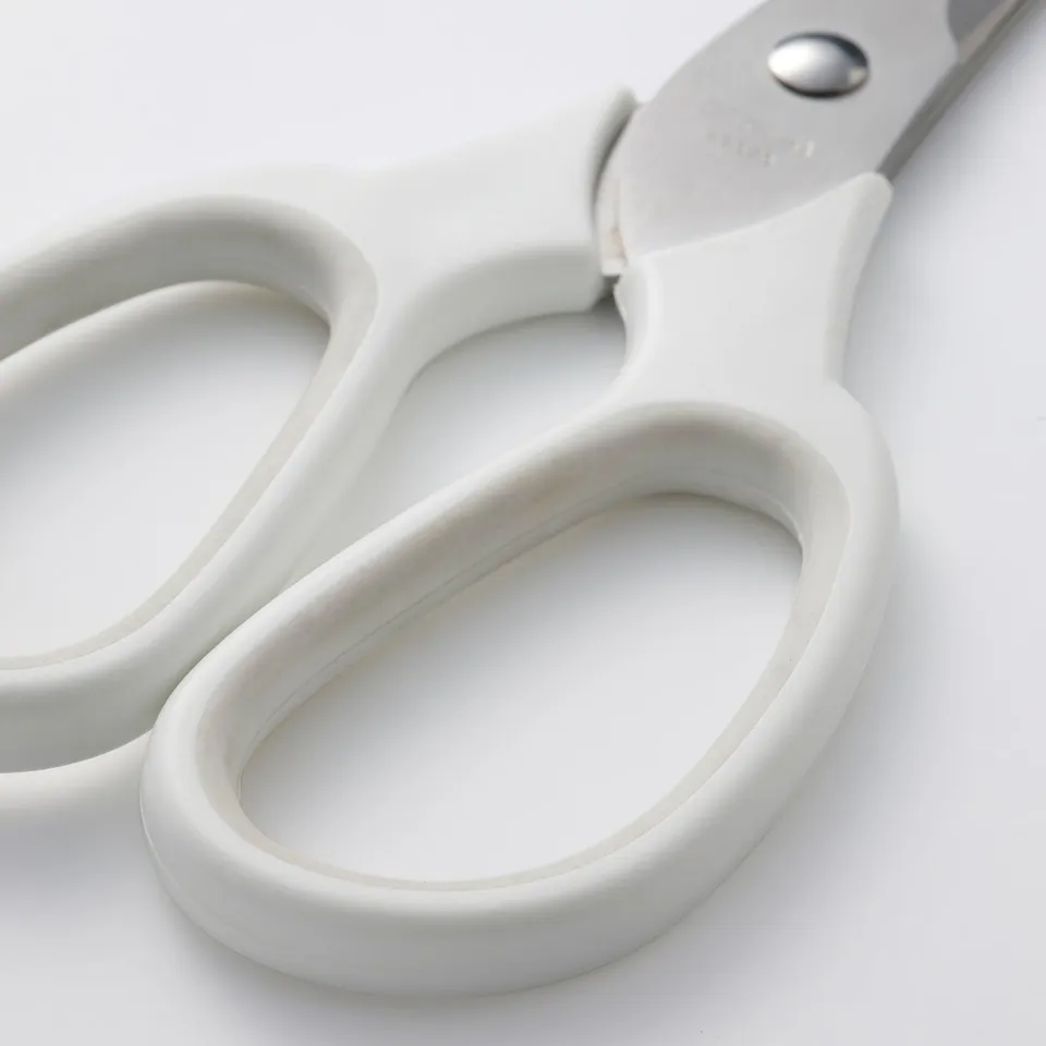 Scissors with smooth, white handles laying open on a white surface. Handles made of durable plastic, blades closed and aligned neatly.