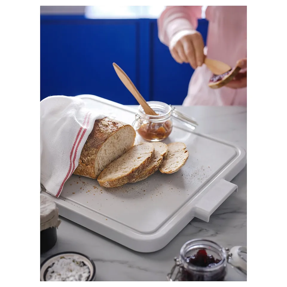 A white LILLHAVET chopping board with bread and a jar of jam on a marble countertop.