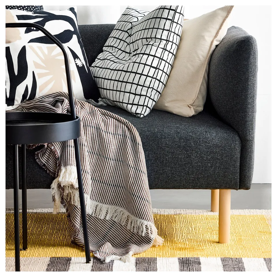 Modern grey sofa with black side table, patterned pillows, stripe blanket, and yellow plaid rug.