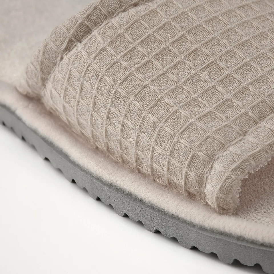 Light beige waffle slippers close-up, soft texture, cushioned sole.