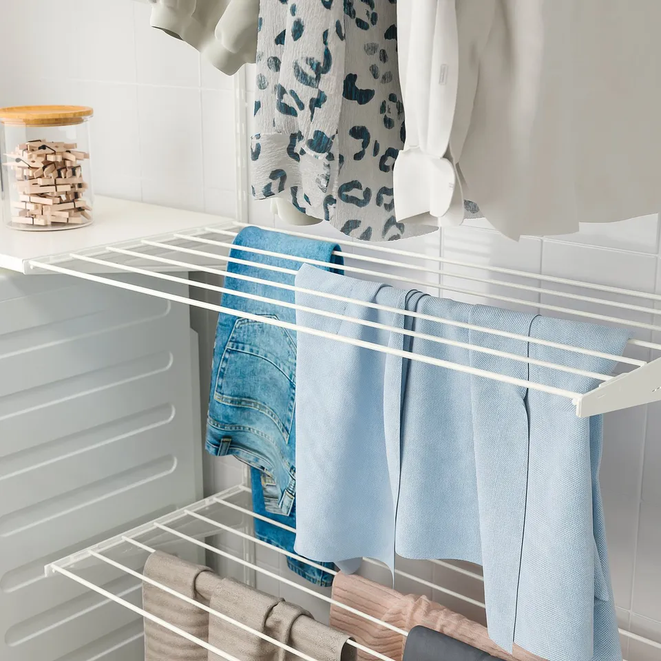A white BOAXEL wall-mounted drying rack holds several blue jeans and light-colored clothes, efficiently organising laundry for drying.