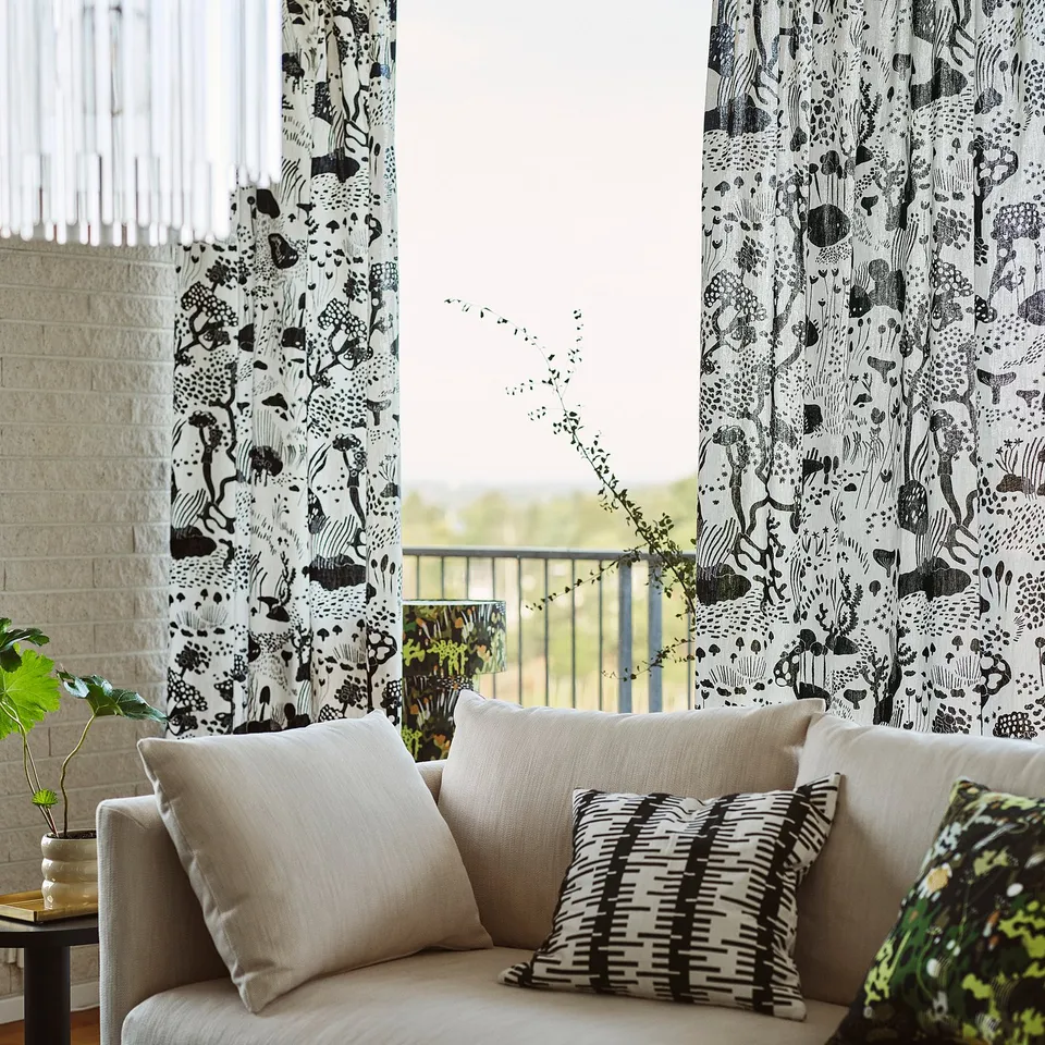 Curtain with black patterns in window, sofa with striped pillows, plant.