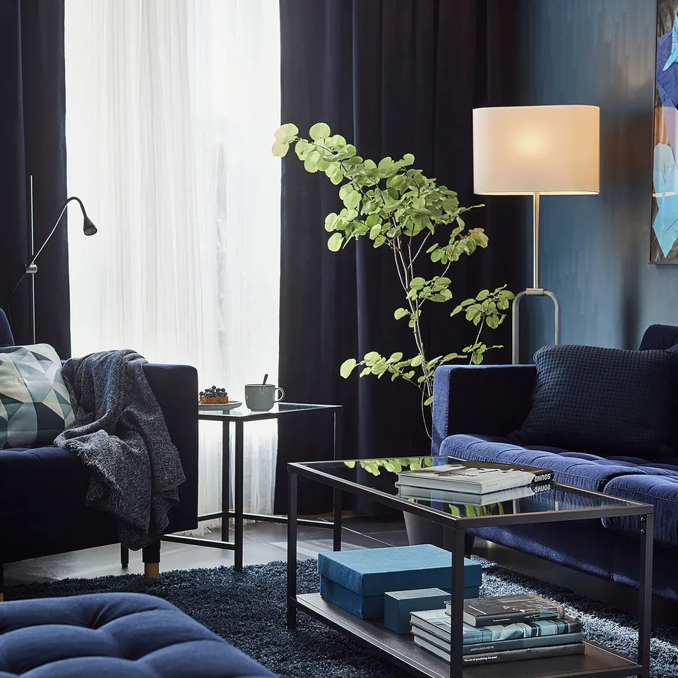 Modern living room with dark blue furniture, coffee table, lamp, and large window.