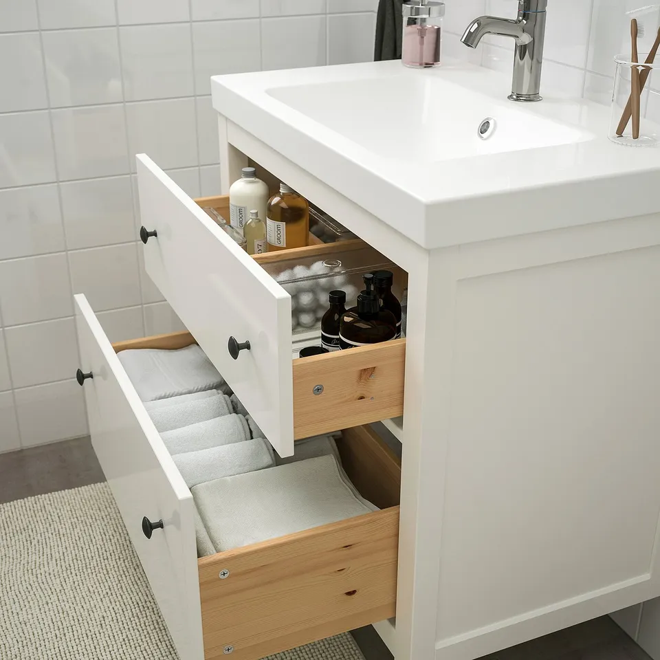 White bathroom vanity with open drawers, storing towels and toiletries, featuring smooth-running drawers and a sink with modern fixtures.