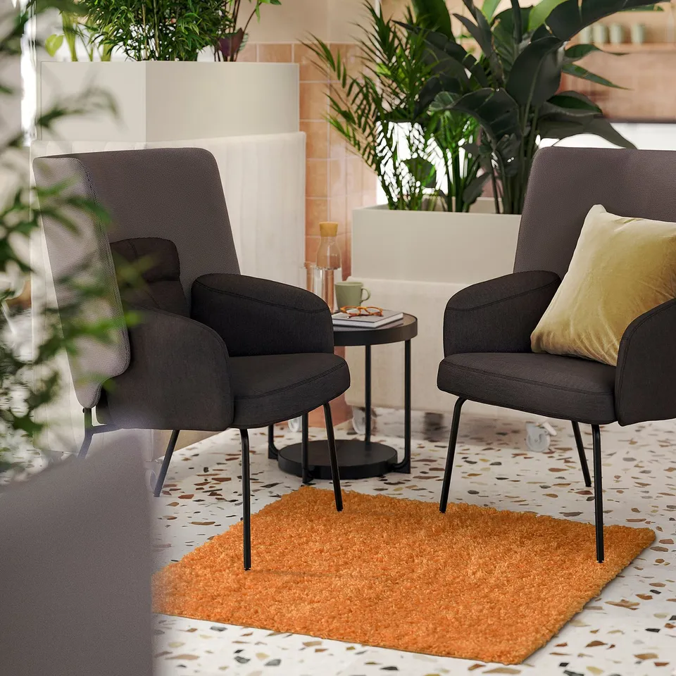 Two grey chairs on orange rug in cosy, plant-filled room.