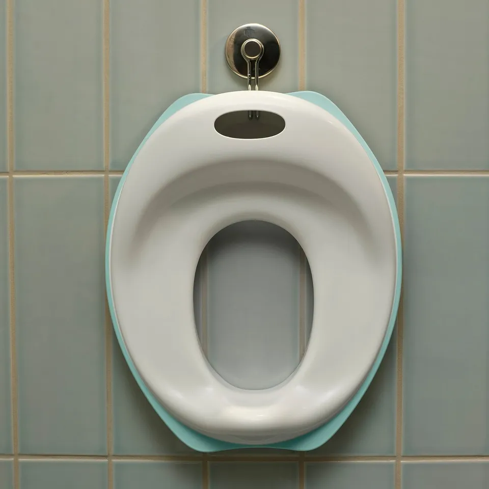 A white and light blue childrens toilet seat with soft curves, attached to a wall with tiles.