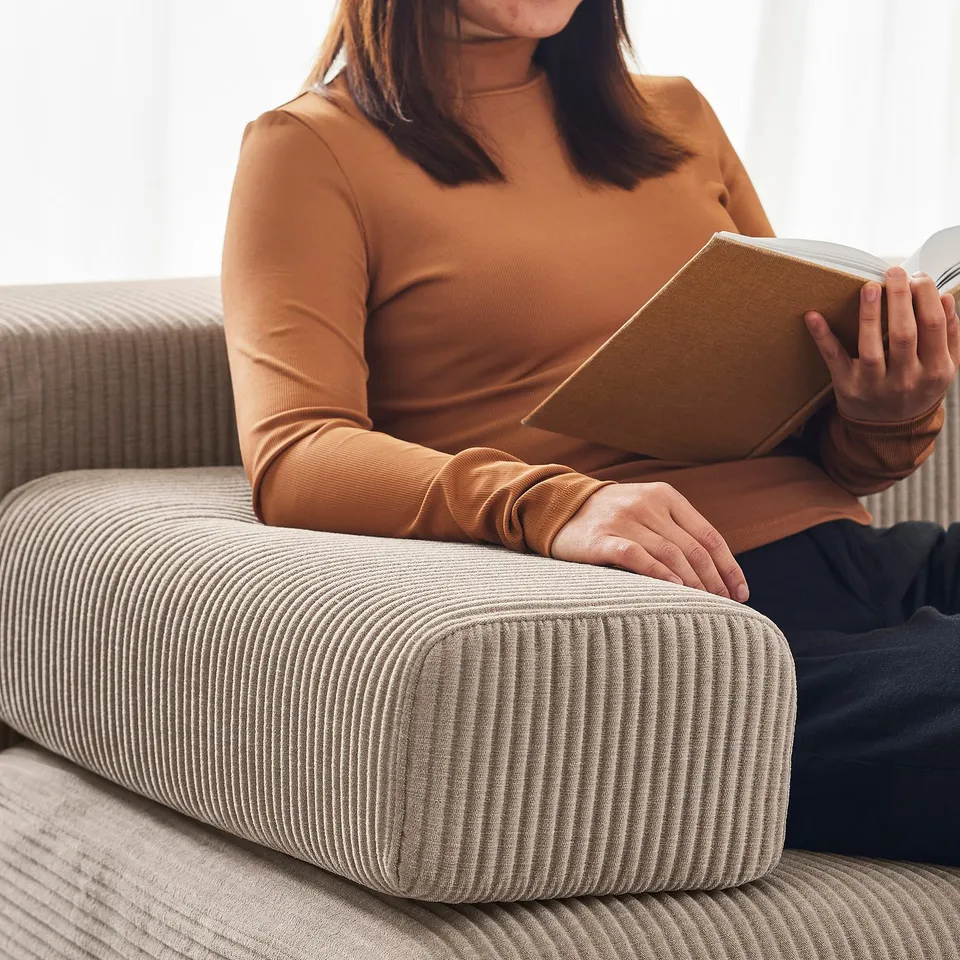 Person reading on a brown JÄTTEBO sofa, wearing a mustard top, sitting comfortably with the cushioned headrest.