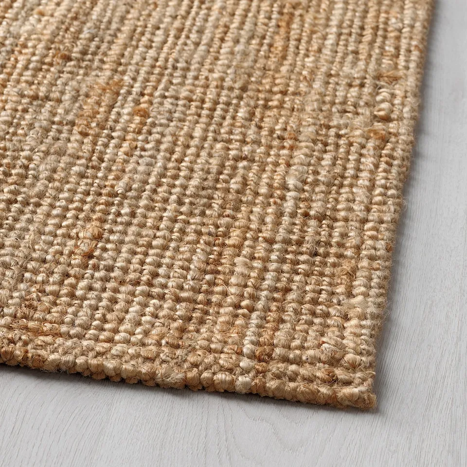 Natural jute rug on light wood floor, showcasing textured weave and earthy tone.