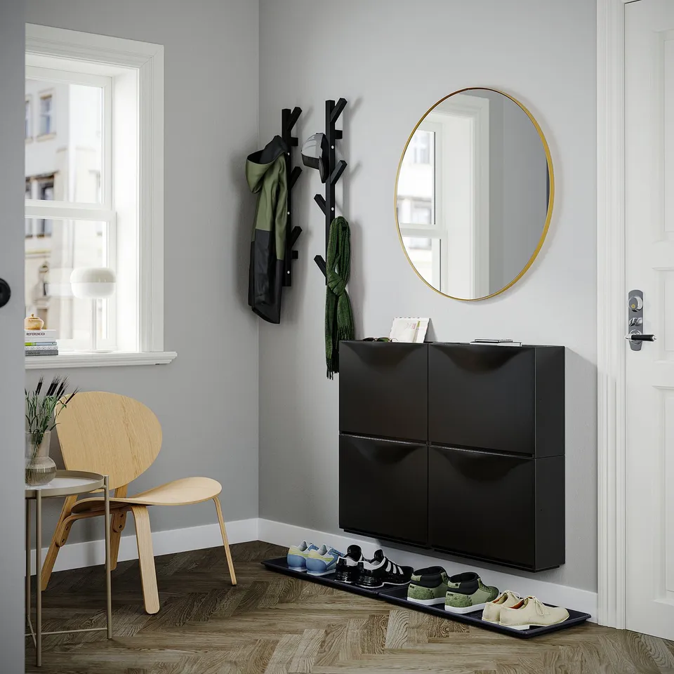 Modern entryway with black gloss TRONES shoe cabinet, round gold mirror, wooden coat hanger, and light wood chair.