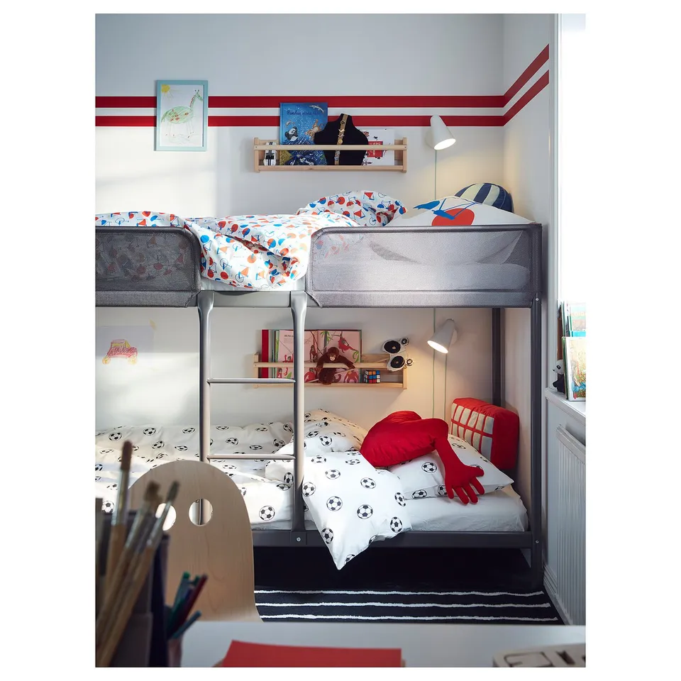 Kids room with grey soccer-themed bunk bed, books, toys, red glove, chair. Black & white rug, wooden chair, colourful walls.