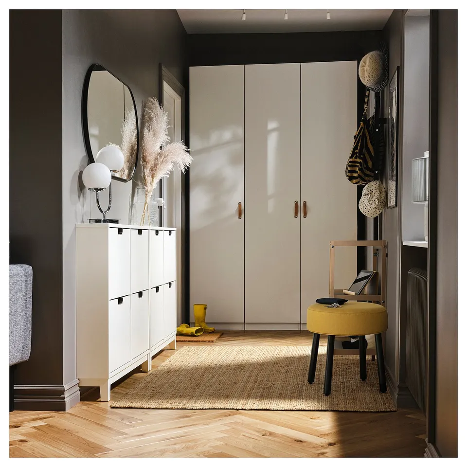 Modern entryway with white cabinets, mirror, yellow stool, rug, and wall hooks.