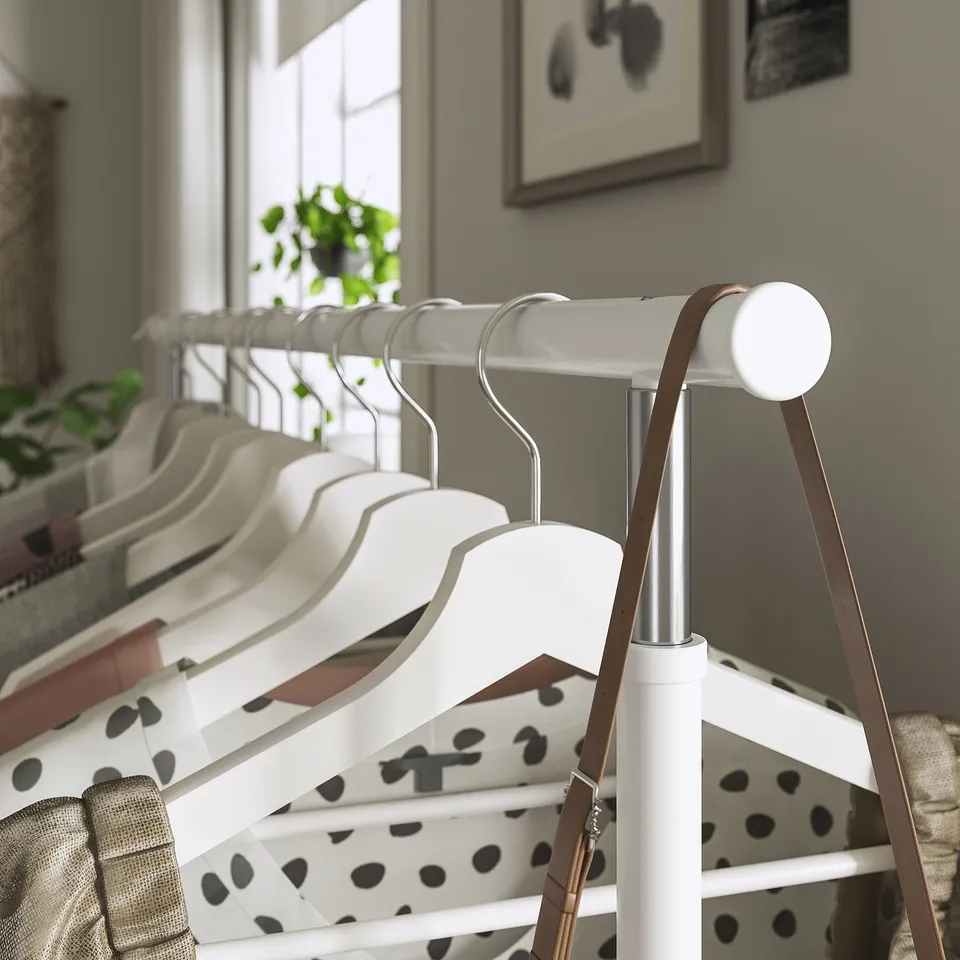 White clothing rack with wooden hangers, adjustable height, near window with plant.