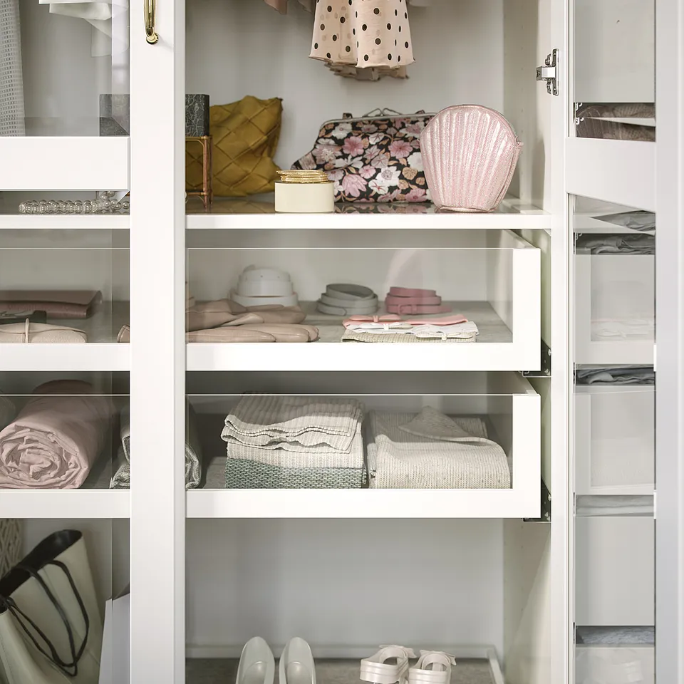 A white wardrobe with glass shelves displays neatly organised clothes and accessories.