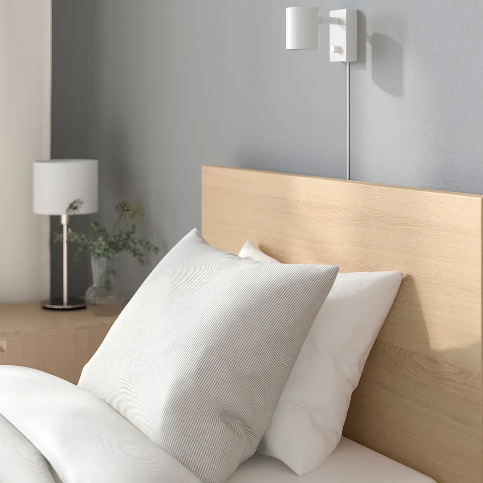 Wooden headboard bed with pillows and lamp. Adjustable bed sides and high headboard for comfort.