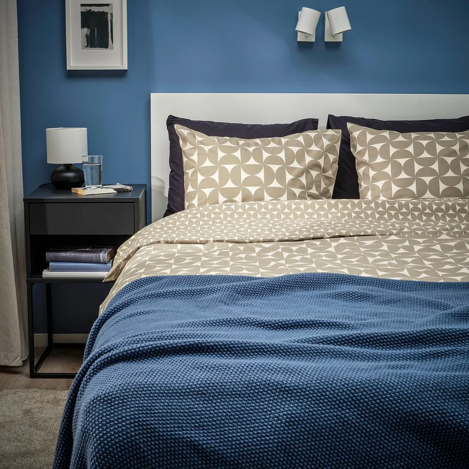 Modern bedroom with ÄNGSNEJLIKA duvet, geometric pattern, blue accents, bedside table, and wall art.