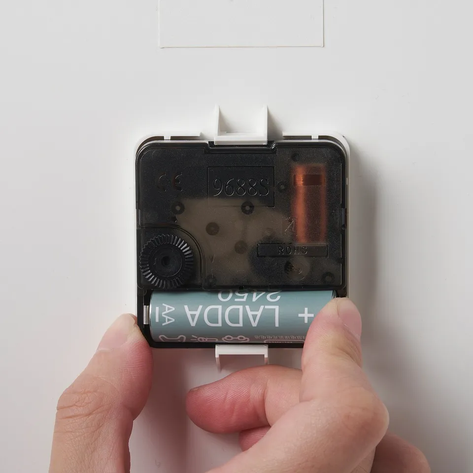 Hands placing battery into silent quartz clock. Clock has clear numbers and no ticking sound.