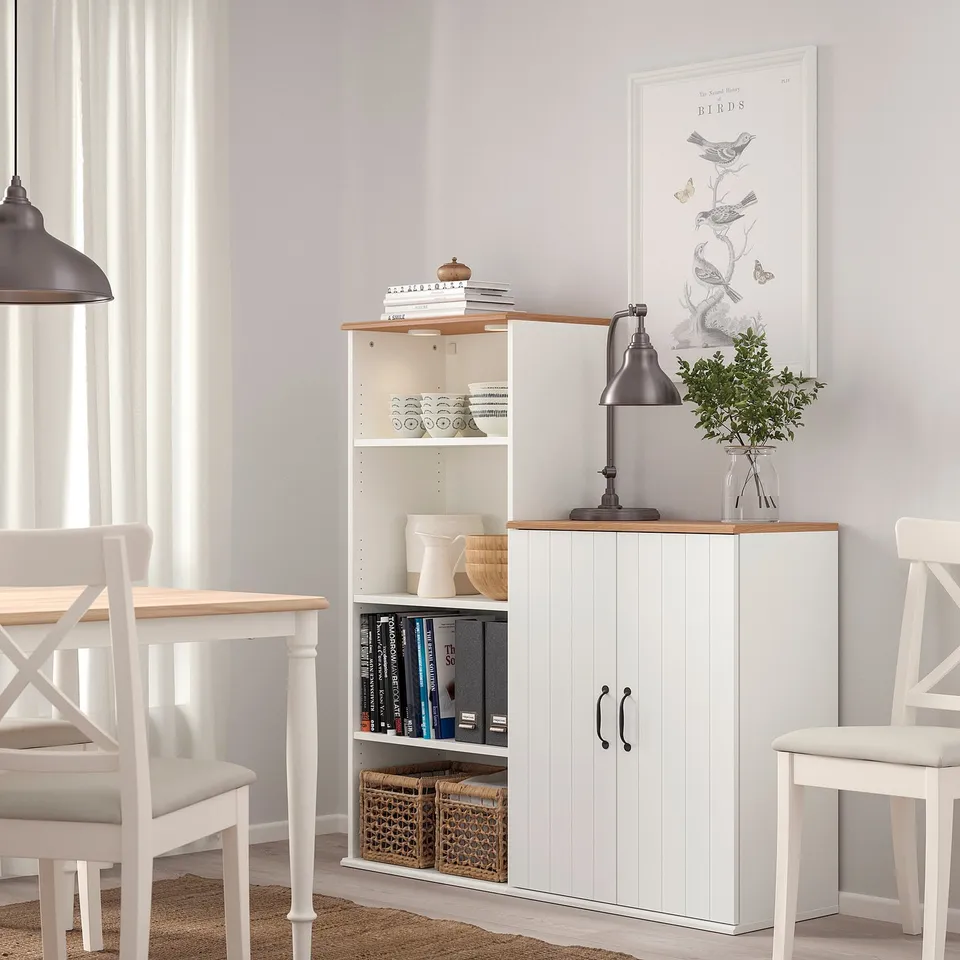 SKRUVBY storage cabinet with books, bowls, lamp in dining area with chairs.