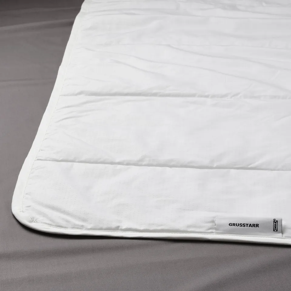 White duvet with a subtle dot pattern neatly placed on a grey bedsheet.