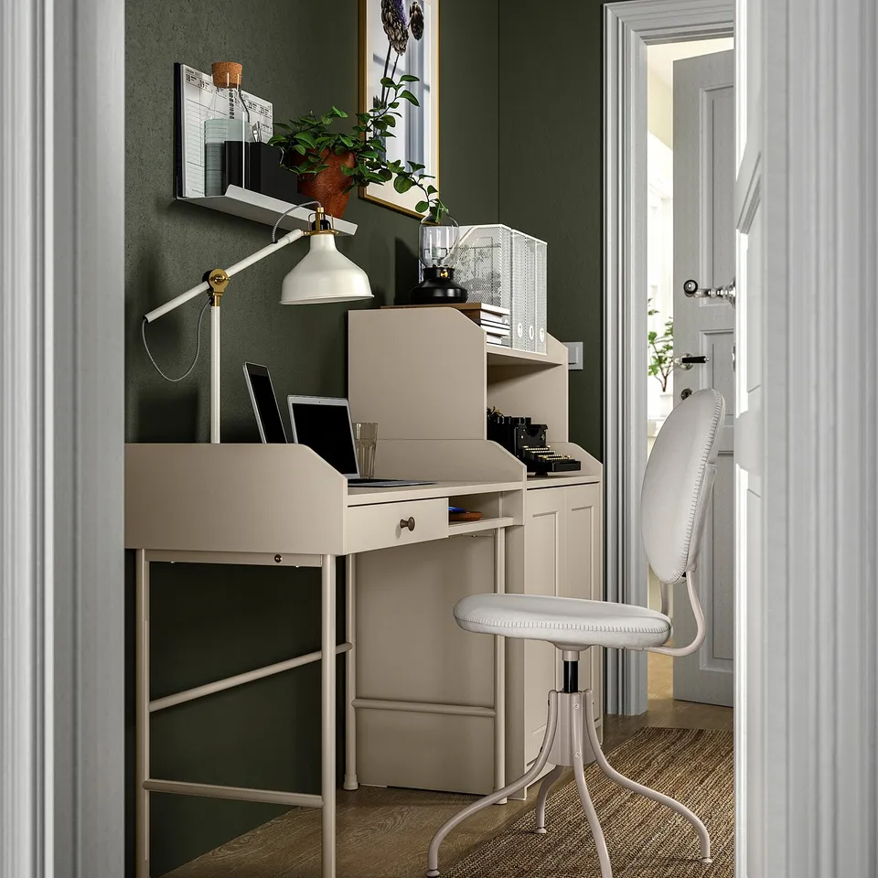 Home office setup with white desk, adjustable lamp, potted plant, laptop, and chair against green wall.
