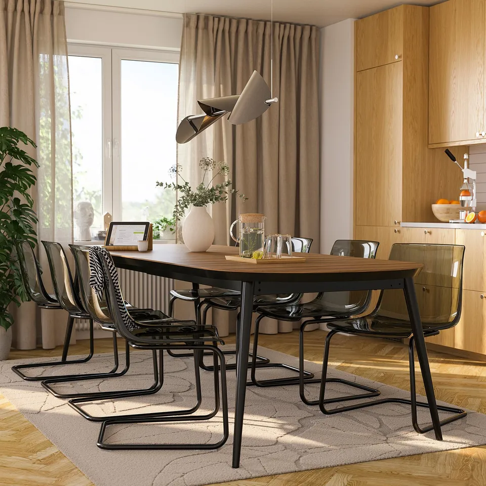 Expandable dining table in modern kitchen with walnut top and steel frame, seating 4-8, with hanging lights and transparent chairs.