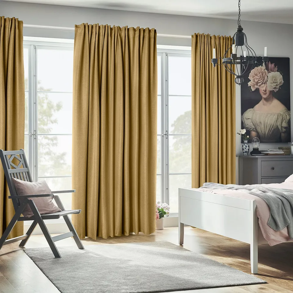 Bedroom with ANNAKAJSA mustard curtains, large chandelier, grey bed, and chair. Curtains are floor-length, covering tall windows.