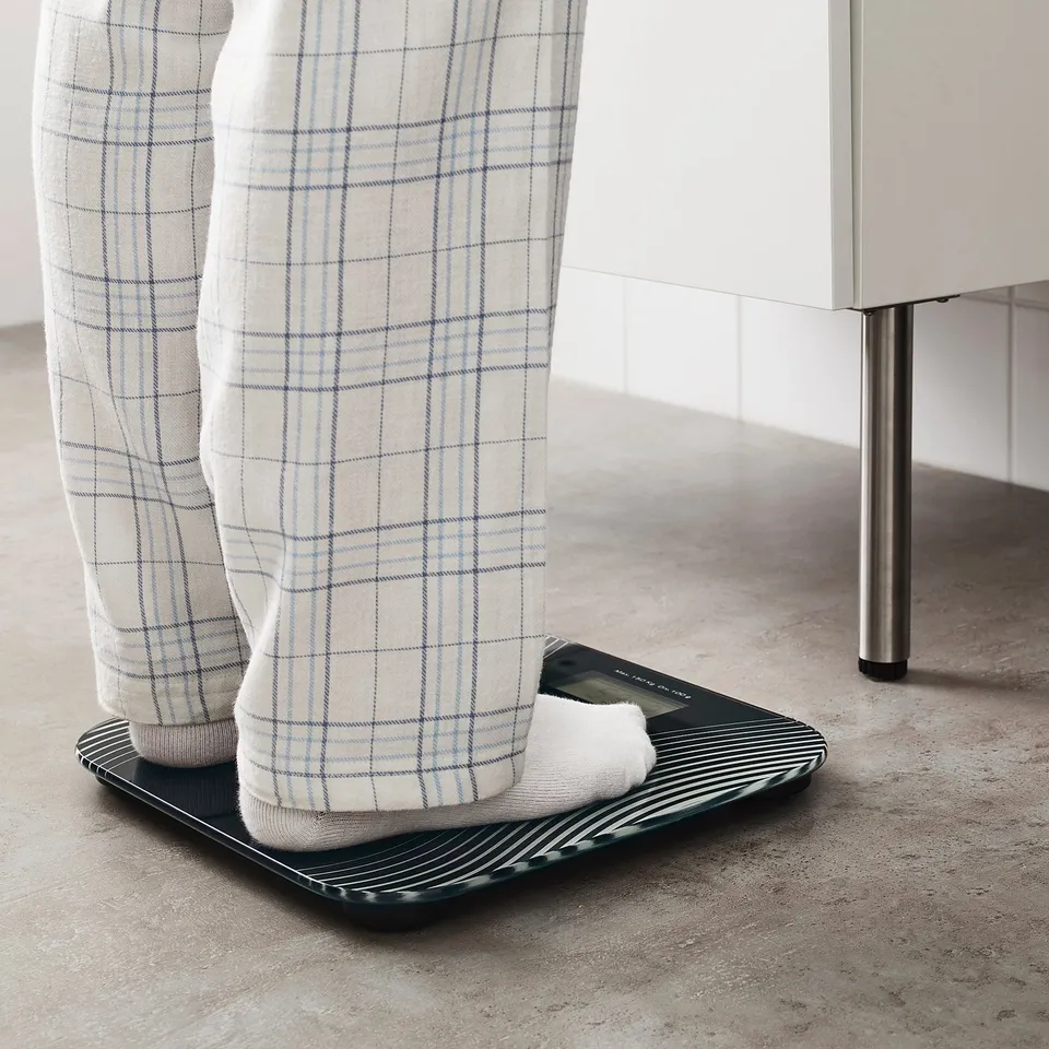 Person standing on black digital scale, wearing chequered pyjama pants.