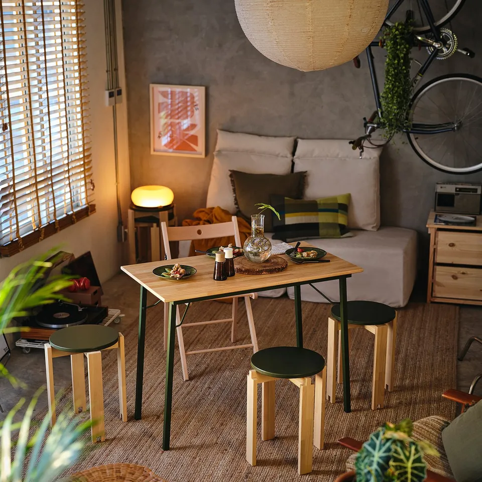 Stackable wooden stools around table with plates, grey sofa, bicycle.
