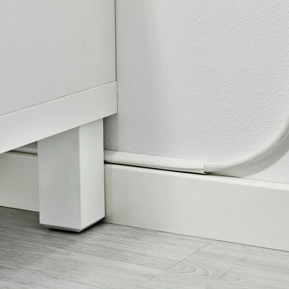 White cable trunking fixed along skirting board, managing and concealing wires neatly.