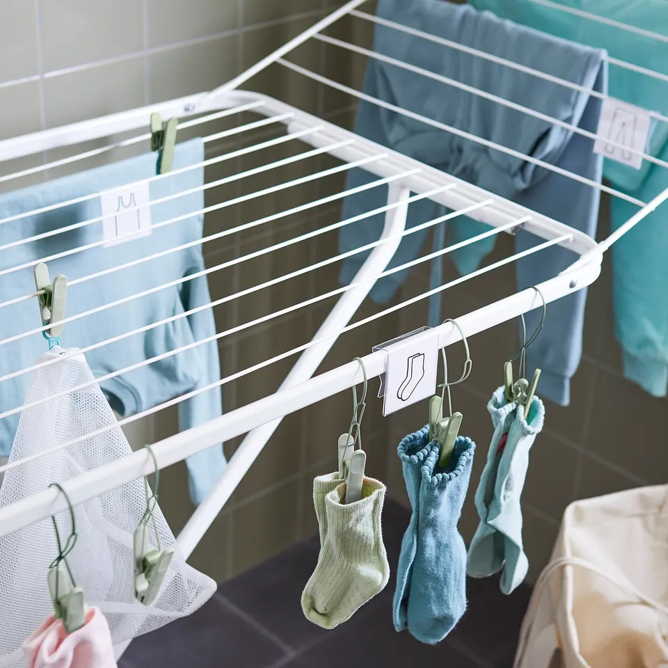 White MULIG drying rack with two wings holds laundry. Clothespins secure socks and clothes.
