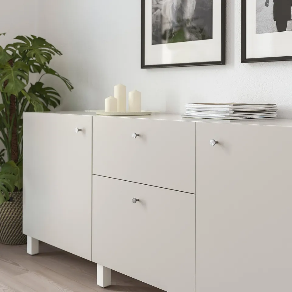 White storage cabinet with two drawers and two doors, silver handles, and candles on top.
