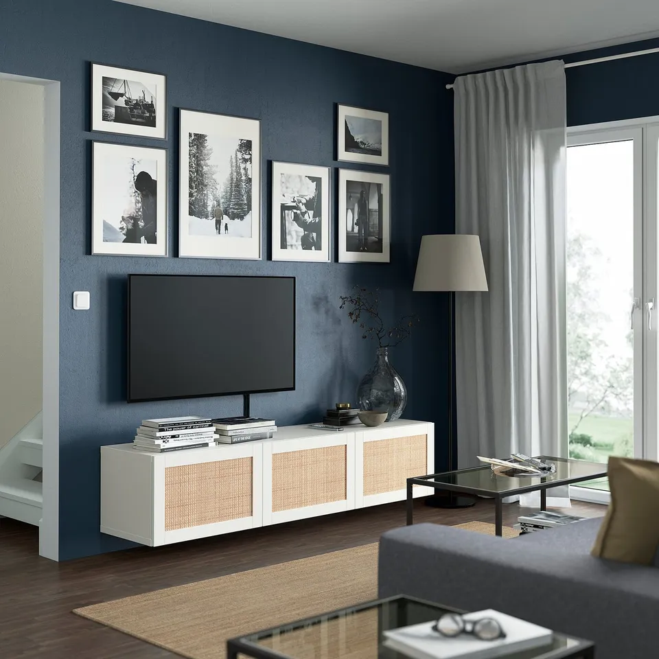 Modern living room with BESTÅ tv bench, dark blue wall, white stand, grey sofa, flat-screen tv, glass table, and curtains.