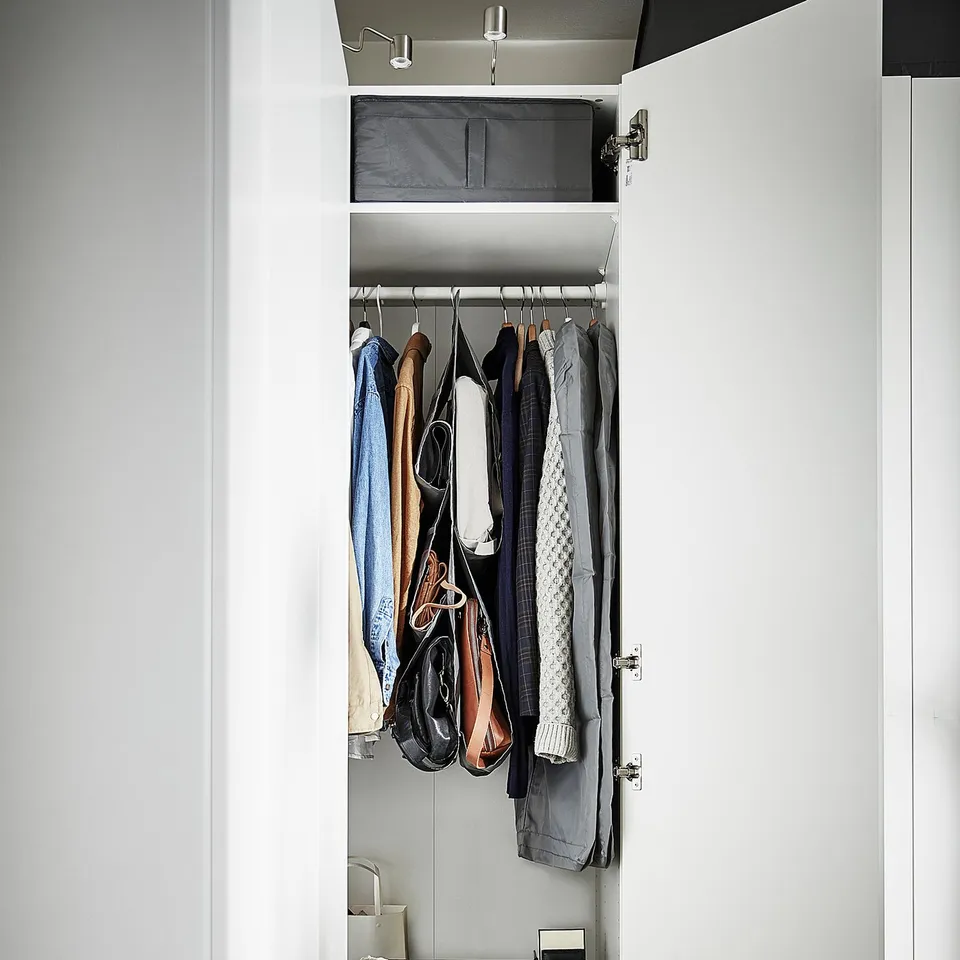 A white closet with clothes: suits, bags, and a box on the top shelf. Lower shelves have folded clothes and a box.