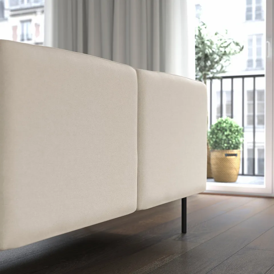 Modern, light beige modular sofa with clean lines, positioned near a window with city views and a potted plant.