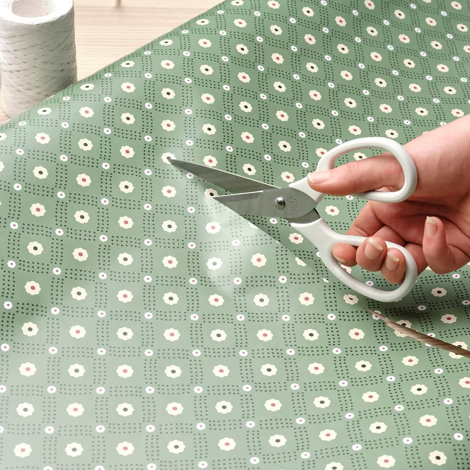Person cutting green patterned paper with floral scissors.