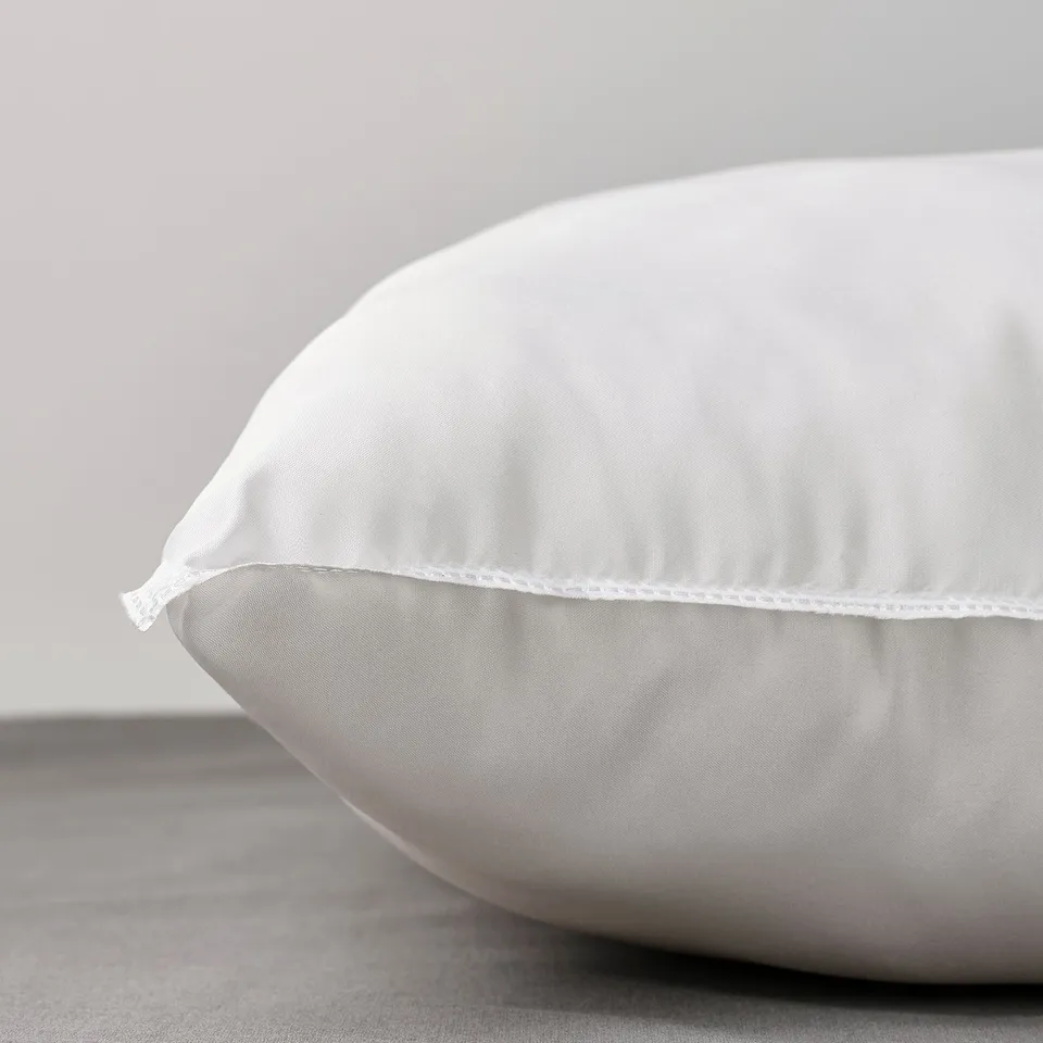 Close-up of plush, white pillow on grey surface, showcasing soft fabric and detailed stitching.