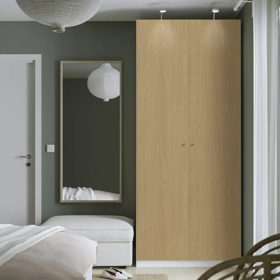 Modern bedroom with tall wooden wardrobe, mirror, bed, and hanging lights.
