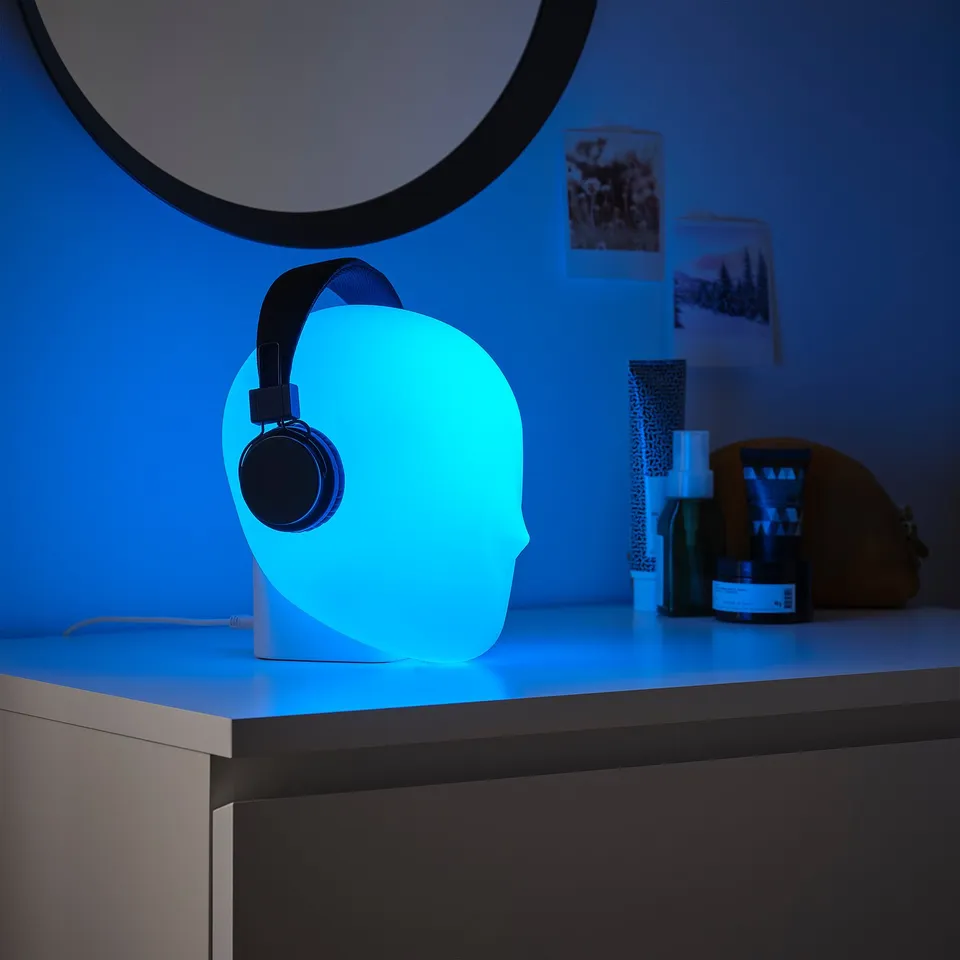 ISKÄRNA lamp in blue, shaped like a head with headphones, on a desk with mirror and toiletries.