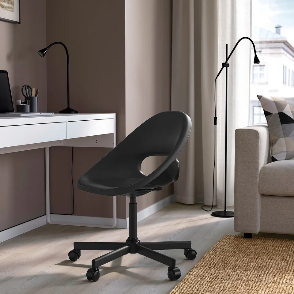 Modern black plastic desk chair with adjustable height and castors, positioned under a white desk with a laptop, complementing minimalist decor.