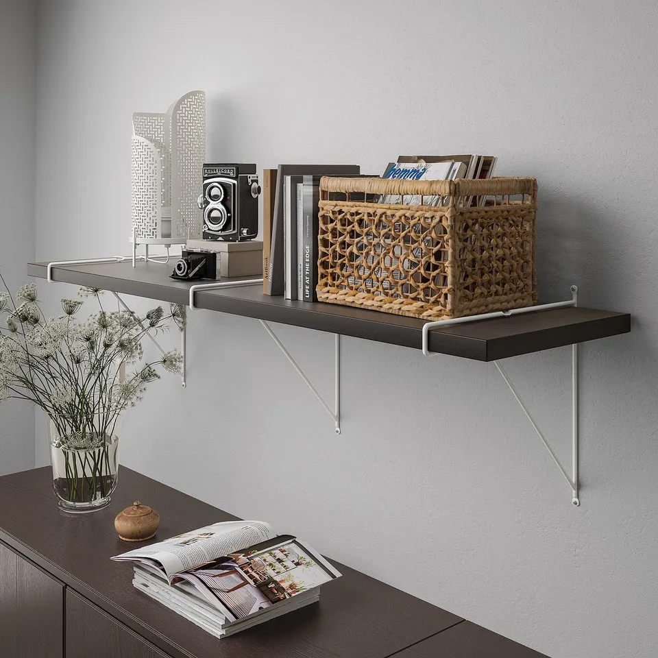 A wall-mounted dark-colored shelf with angled brackets, holding magazines, books, and a camera, showcasing storage and display functionality.
