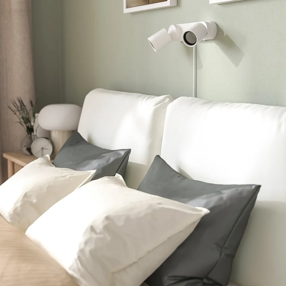 A white bed frame with two large pillows leans against a wall, featuring a modern and inviting design, perfect for relaxation and reading.