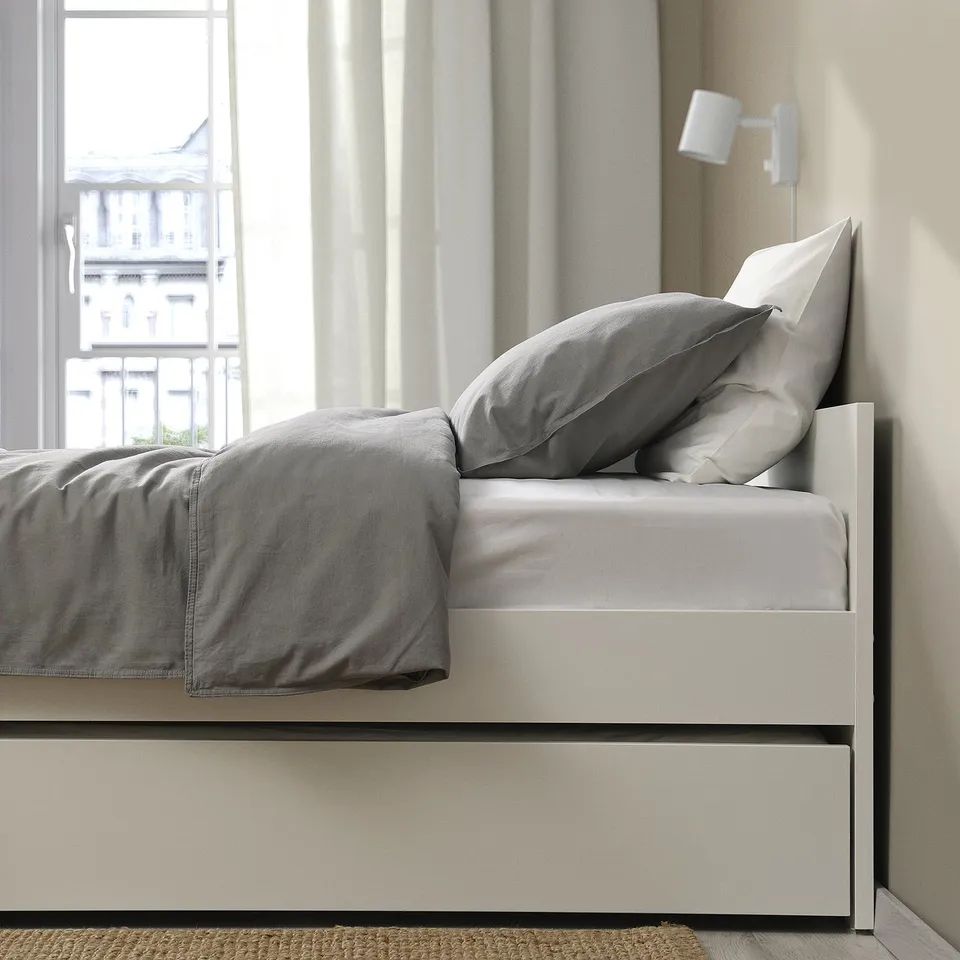 Modern bed frame with trundle, grey bedding, wall-mounted light. Clean, minimalist design.