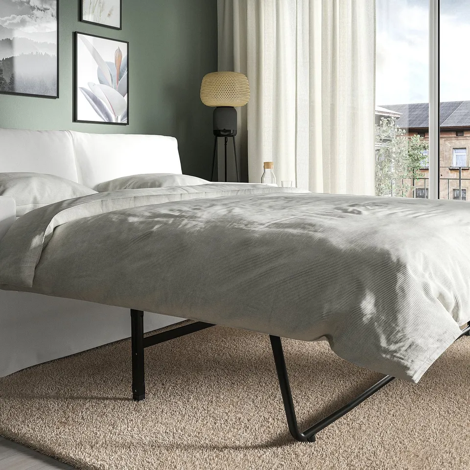 Bed in modern room, grey comforter, white headboard, black metal frame, tripod lamp, large window, city view.