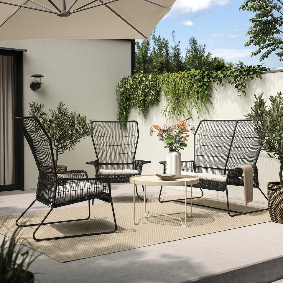 Modern outdoor patio set: black metal and wicker furniture with cushions, white coffee table, and umbrella.