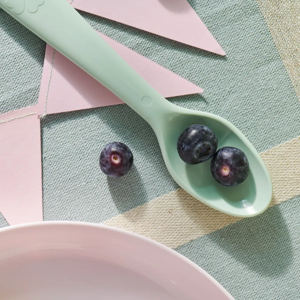 Kids spoon with purple fruits on pastel mats.