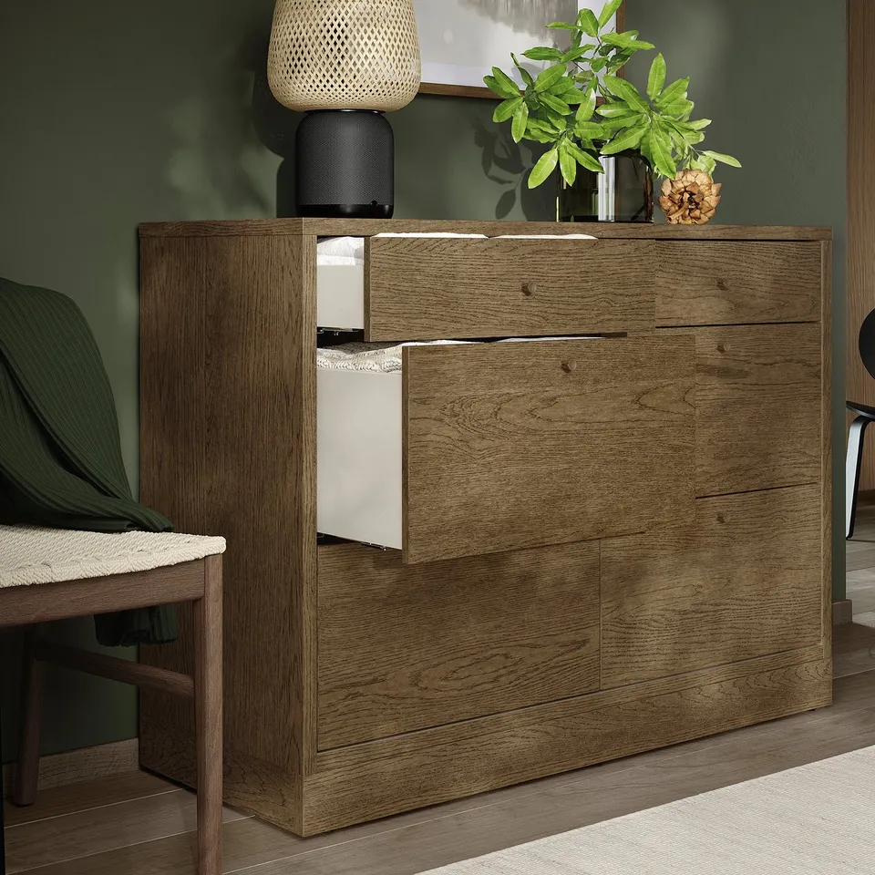 Brown wood chest with drawers, one open, green wall, plants, lamp.